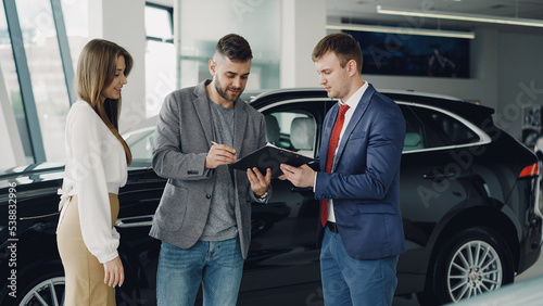 Handsome young guy is signing sale and purchase agreement in car dealership