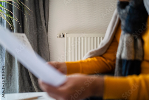 Man holding heating bill with radiator mounted on wall at home