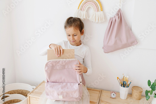 Cute girl removing book from backpack sitting on table photo