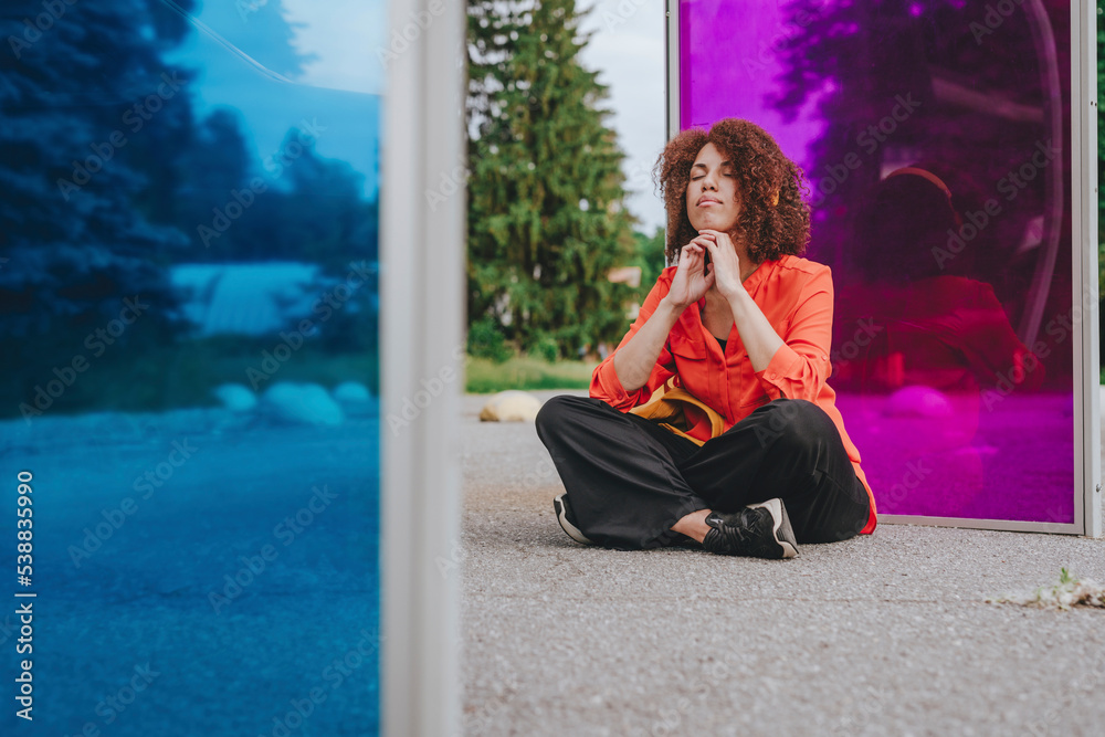 Young woman with eyes closed and hands on chin sitting in front of magenta glass Young woman with eyes closed and hands on chin sitting in front of magenta glass