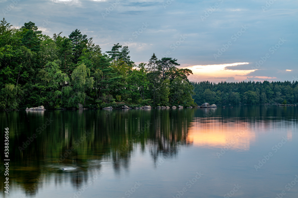 Scenic view of calm lake and trees in forest against cloudy sky during sunset