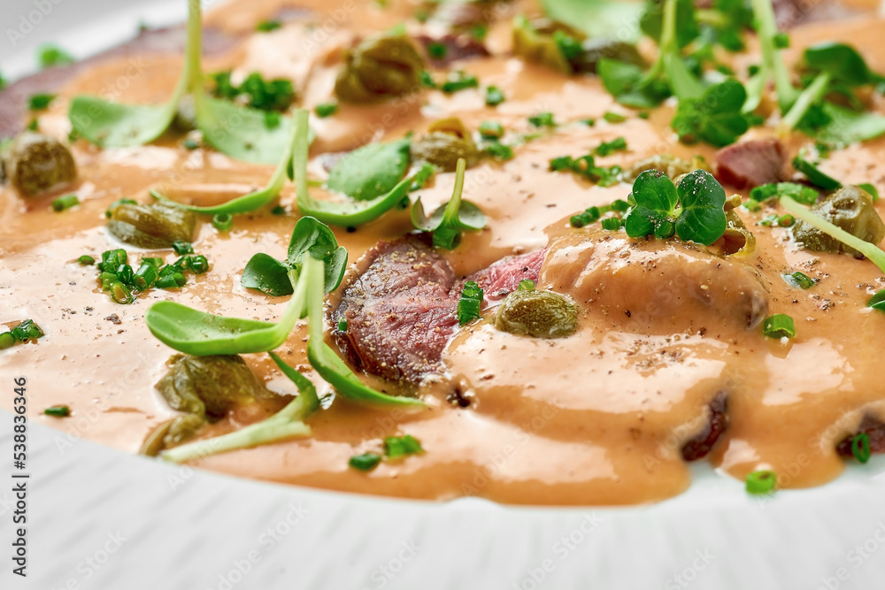 Vitello tonnato from veal with sauce in a white plate on a white background. Close-up, selective focus.
