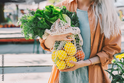 Customer holding leafy vegetables and lemons in mesh bag at local market photo