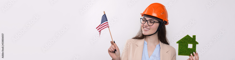 A girl in a construction helmet and an American flag holds a green eco house.