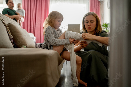 Mother helping daughter putting on tights at home photo