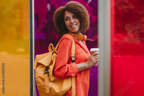 Smiling woman with backpack and disposable coffee cup by vibrant color glasses