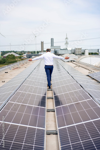 Businessman with arms outstretched walking amidst solar panels on rooftop