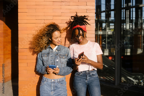 Young woman sharing smart phone with friend on sunny day photo