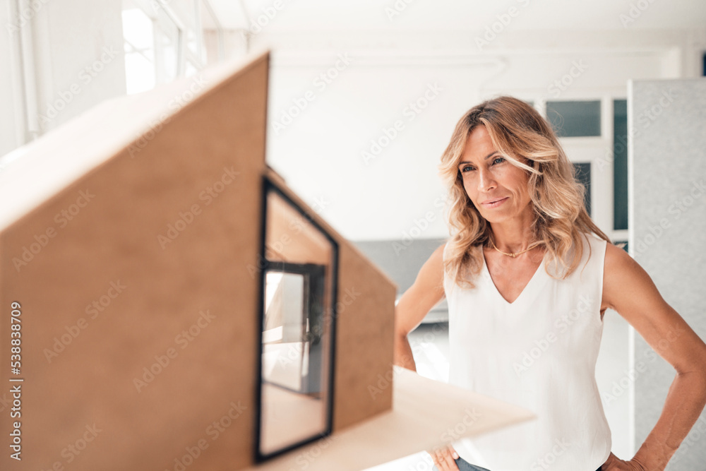 Architect with hand on hip looking at house model Architect with hand on hip looking at house model
