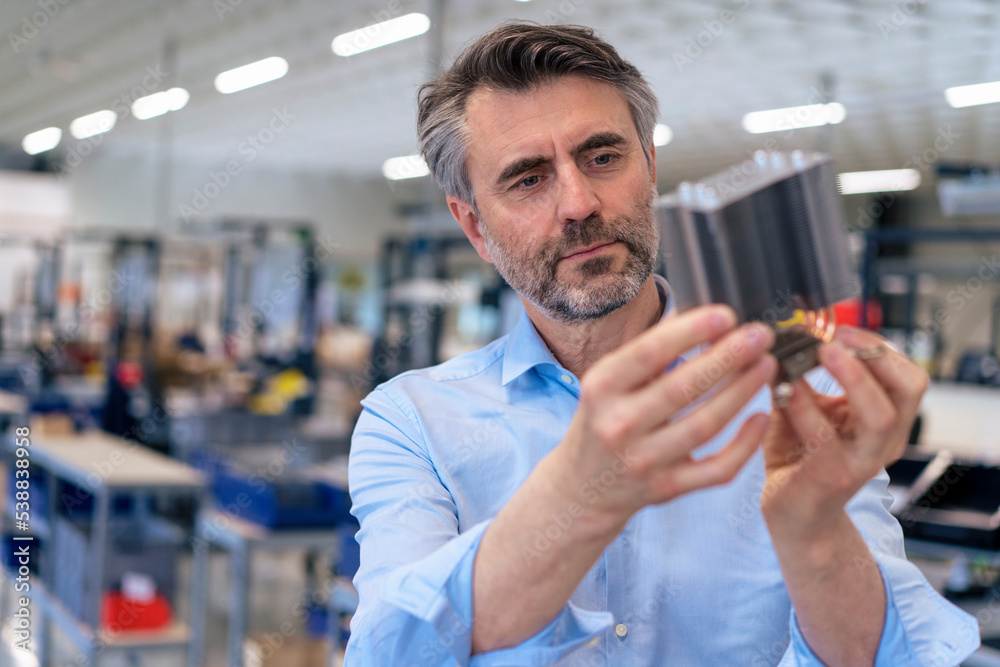 Mature businessman examining machine part in industry Mature businessman examining machine part in industry