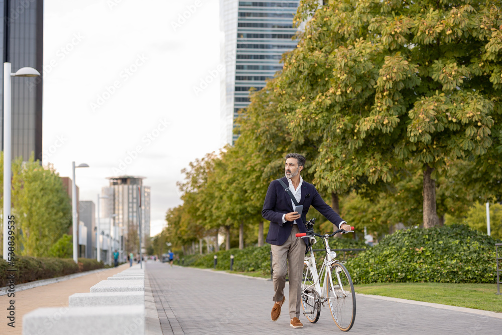 Businessman wheeling with bicycle on footpath Businessman wheeling with bicycle on footpath