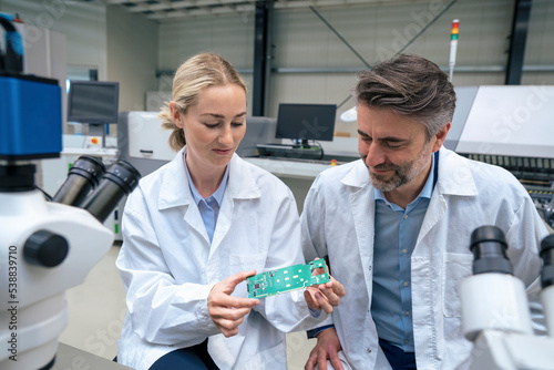 Smiling scientists examining circuit board sitting in industry photo