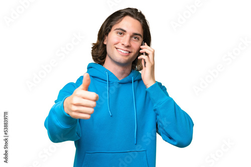 Young handsome man isolated on green chroma background keeping a conversation with the mobile while doing thumbs up © luismolinero