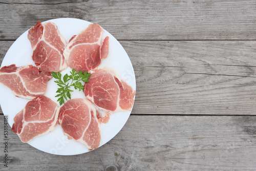 Raw Pork Slice in White Round Plate on old Wooden Table. Slide raw meat on the table decorated with parsley on a white plate