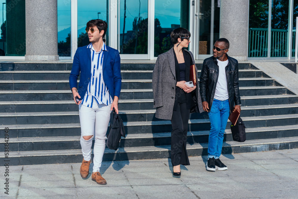 Obraz premium Young modern multi-ethnic people in formal wear discussing business while walking outside the office building
