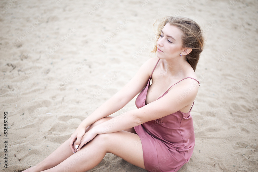 Young woman in pink dress sitting on sand and enjoys sea. Young woman in pink dress sitting on sand and enjoys sea.