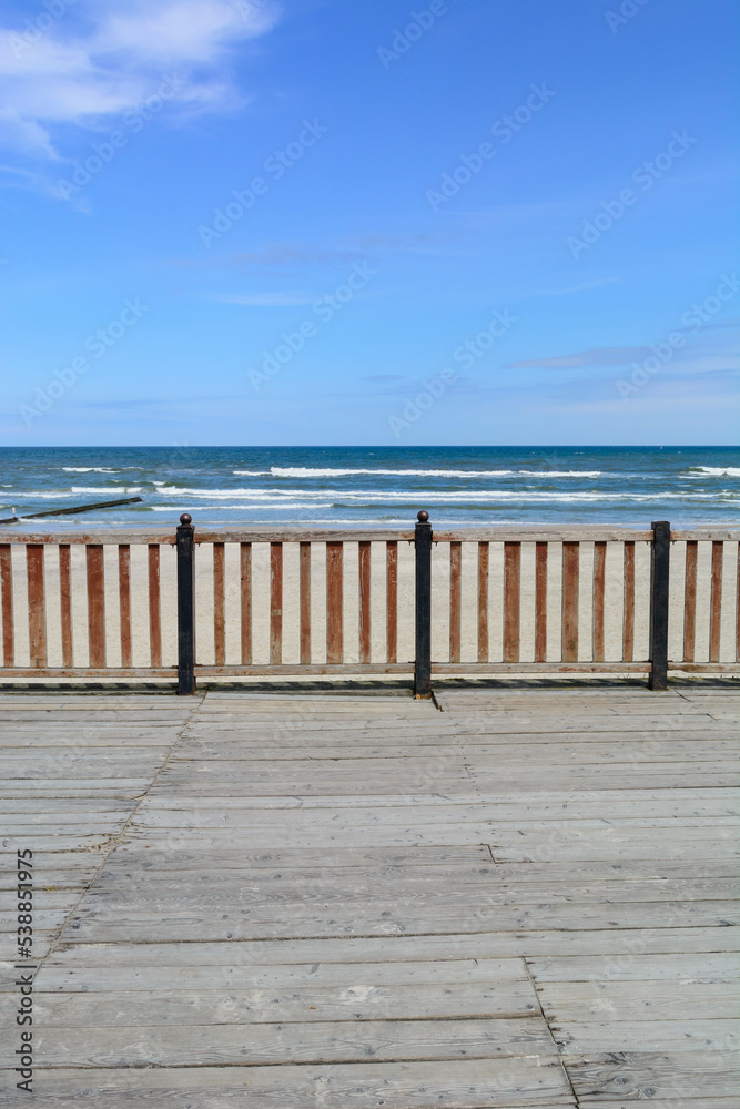 The pier is fenced in front and rear with a orange, wood fence. In the background there is a blue sea and a bright sky.