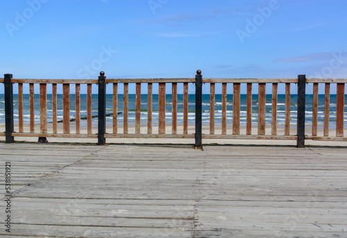 The pier is fenced in front and rear with a orange, wood fence. In the background there is a blue sea and a bright sky.