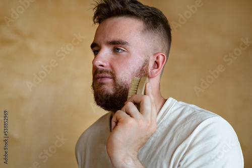 Portrait brutal handsome bearded man with blue eyes holding comb, natural brush, male personal self care, products, accessory for growth style dark brown red beard. Lifestyle people