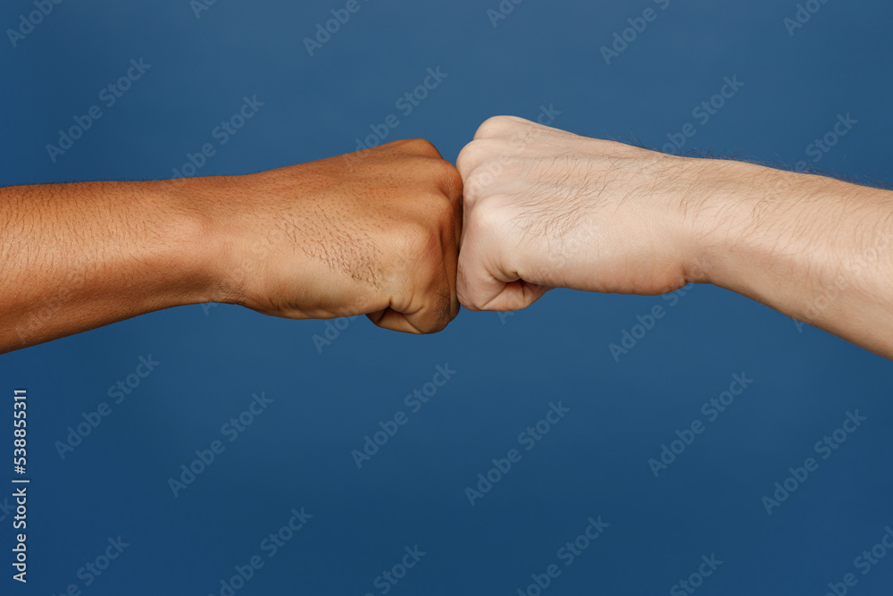 Close up cropped two buddies friends male hands giving fist bump gesture together isolated on plain dark royal navy blue color wall background studio. Teamwork concept. Copy space advertising mock up. Close up cropped two buddies friends male hands giving fist bump gesture together isolated on plain dark royal navy blue color wall background studio. Teamwork concept. Copy space advertising mock up.