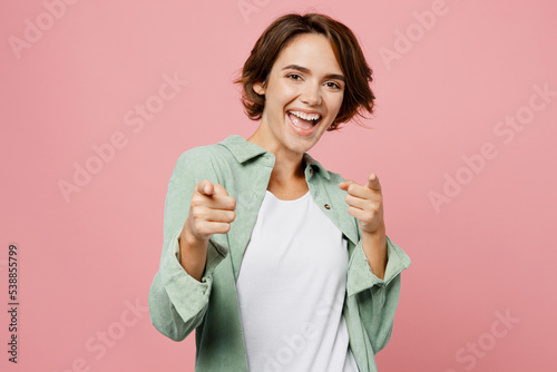 Young confident leader woman she wear green shirt white t-shirt point index finger camera on you motivating encourage isolated on plain pastel light pink background studio. People lifestyle concept.