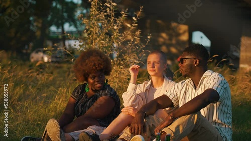 Three friends - two black people and one queer white person enjoying beautiful sunset during outdoor picnic. Diverse group of friends. Summer leisure time activities. High quality 4k footage