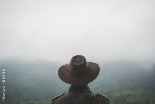Freedom traveler man in hat carrying a backpack stands at the top of a mountain on a foggy day.Adventure travel and success concept photo