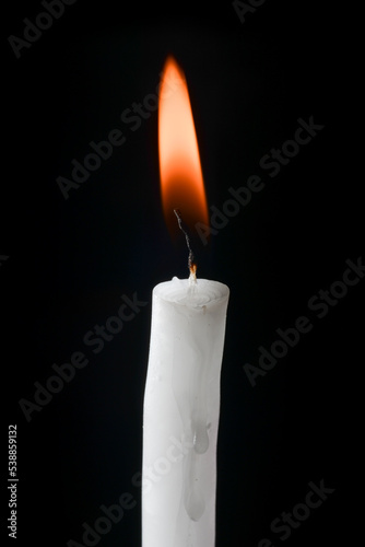 white candle lit with red and yellow flame on black background