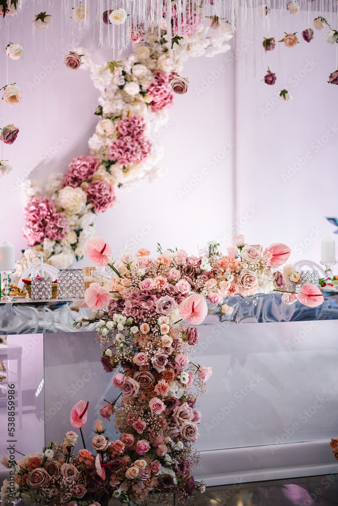 Festive table, arch, stand, garland decorated with a composition of pink  flowers and greenery, candles in the banquet hall. Table newlyweds in the  banquet area at the wedding party. Stock Photo