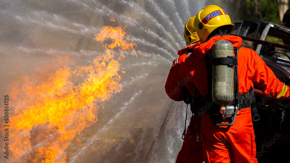 Obraz premium Asian firefighter on duty firefighting, Asian fireman spraying high pressure water, Fireman in fire fighting equipment uniform spray water from hose for fire fighting.
