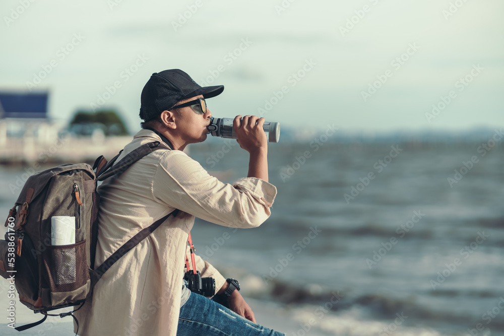 Obraz premium A backpacker sitting to sea watching the sunset and drank his thirst. backpacker concept.