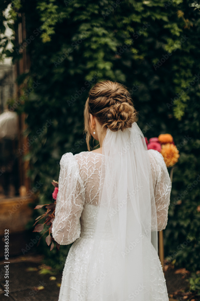 bride in a white wedding dress stands with her back outdoors.