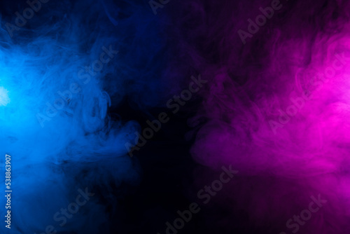 Clouds of colorful smoke in blue and purple neon light swirling on black table background with reflection