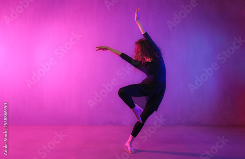 Fototapeta Naklejka Na Ścianę i Meble -  Modern dance girl dancer dancing in neon light doing gymnastic exercises in studio, copy space.