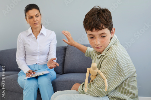 Child having difficulty with communication at therapy session in therapist's or psychologist's office. Upset, unsociable boy refuses help and won't talk to specialist. Mental health problems concept photo