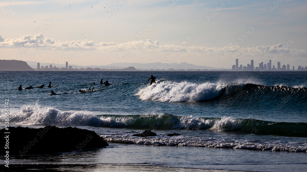 Silhouettes of surfers at sunset with concrete jungle gold coast in the background; surfing in queensland, australia