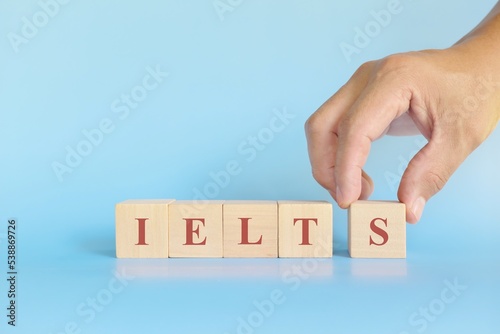 IELTS or international english language testing system exam or test concept. Wooden blocks typography flat lay on blue background.