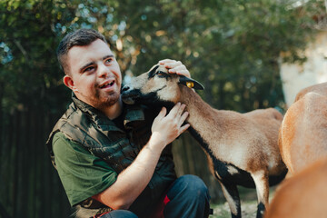 Caretaker with down syndrome taking care of animals in zoo, stroking goat. Concept of integration people with disabilities into society.