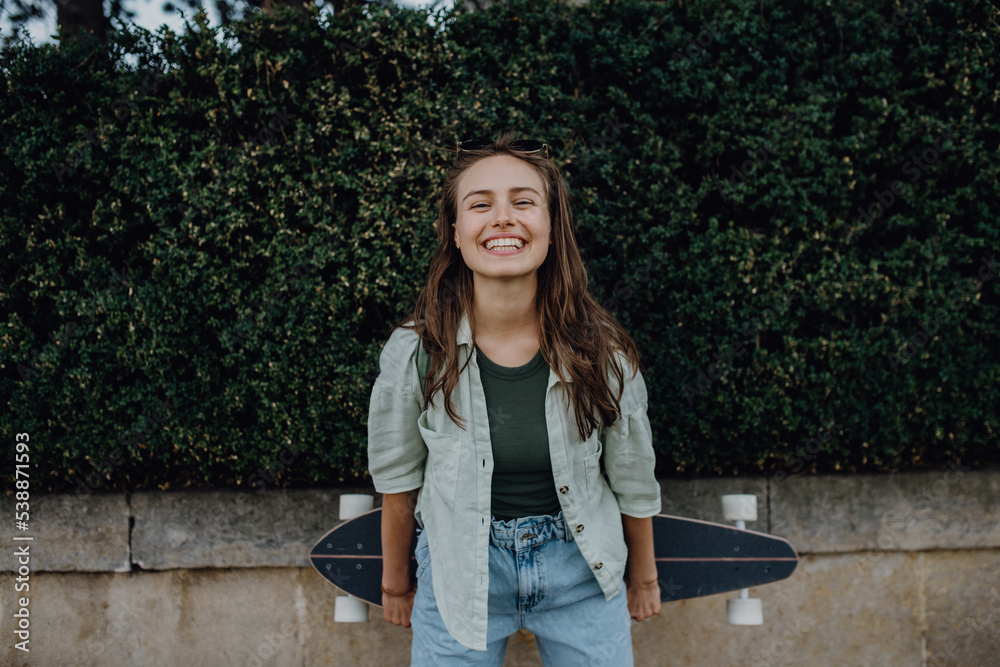 Portrait of young happy woman outdoor with skateboard. Youth culture and commuting concept.