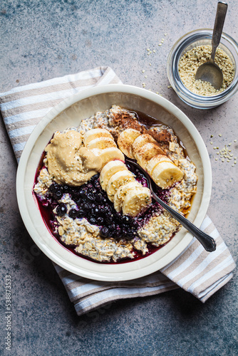 Winter breakfast concept. Overnight oatmeal with banana, berry, chia seeds, sesame tahini, cinnamon and syrup in a bowl, dark background.