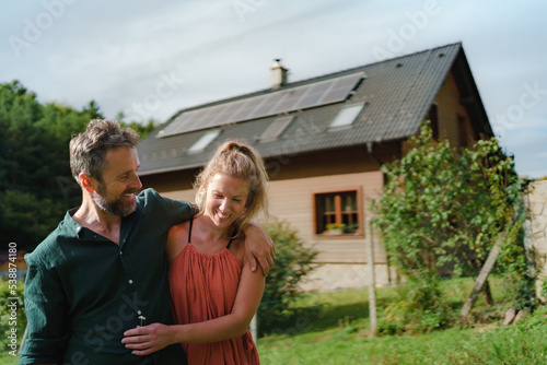 Happy couple standying near their house with solar panels. Alternative energy, saving resources and sustainable lifestyle concept. © Halfpoint
