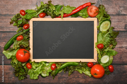 Empty black board surrounded by organic vegetables on wooden table. Healthy eating background