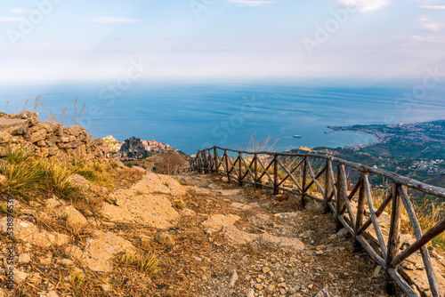 mountain landscape with a hiking trail leading to a mountain town and beautiful blue seashore far away