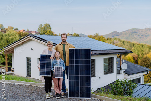 Happy family near their house with solar panels. Alternative energy, saving resources and sustainable lifestyle concept.