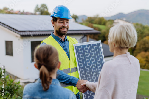 Foto Smiling handyman, photovoltaics panels installer shaking hand with family owner of house