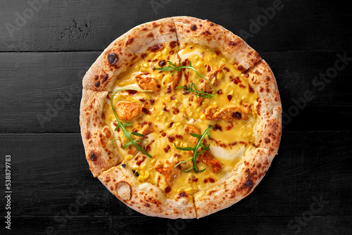 Pizza with cream cheese sauce, chicken fillet, corn, mozzarella and cheddar on black wooden surface