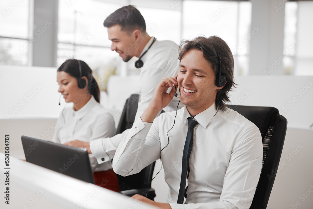 Positive male call center agent working in office near colleagues Positive male call center agent working in office near colleagues