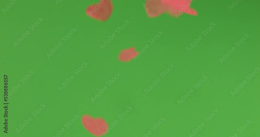 Falling heart-shaped confetti on a green background.