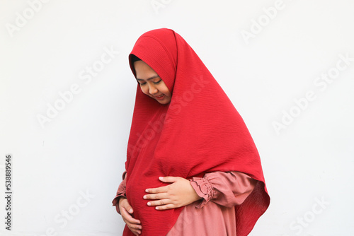Pregnancy and Islam Concept. Beautiful pregnant muslim woman in hijab touching her belly, posing over white background with free space
