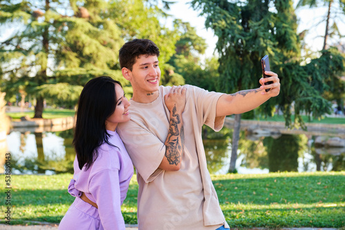 Two young latin friends taking selfie with the smartphone and smiling at street in a park.